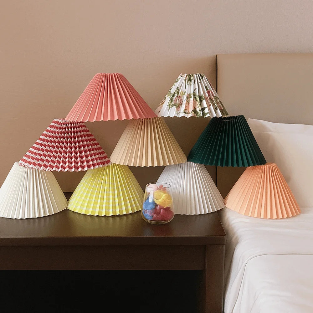 Assortment of colorful pleated lamp shades displayed next to a bed