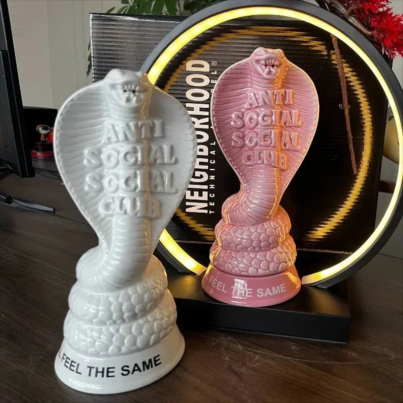 White and pink ceramic cobra incense holders on a table, showing sculptural snake design