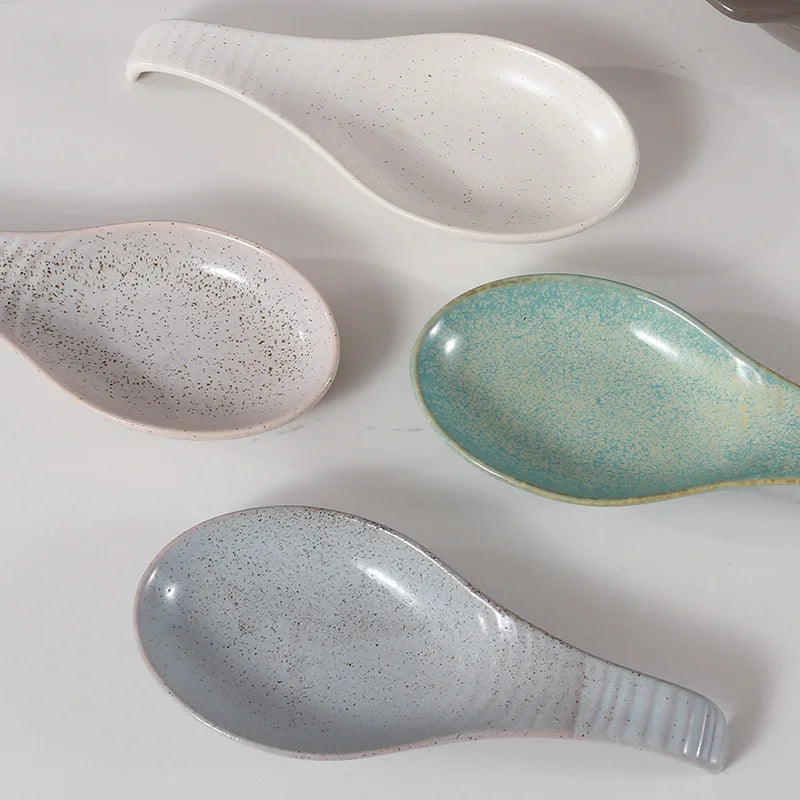 Four ceramic spoon rests in white, gray, green, and beige, arranged on a countertop