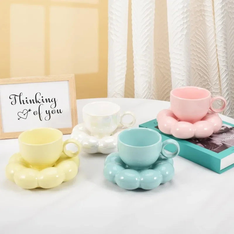 Pastel pink, blue, yellow, and white cloud ceramic mugs on saucers beside a book and a 'Thinking of you' sign