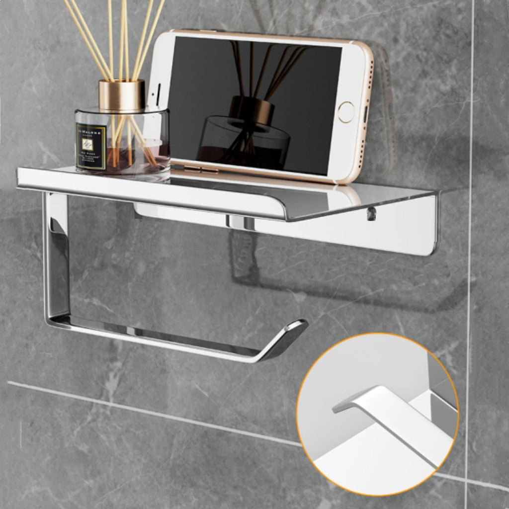 Wall-mounted silver toilet paper holder with integrated flat shelf, styled with phone and diffuser