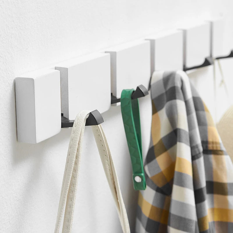 White foldable wall hook rack with several hooks extended, holding bags and a plaid shirt