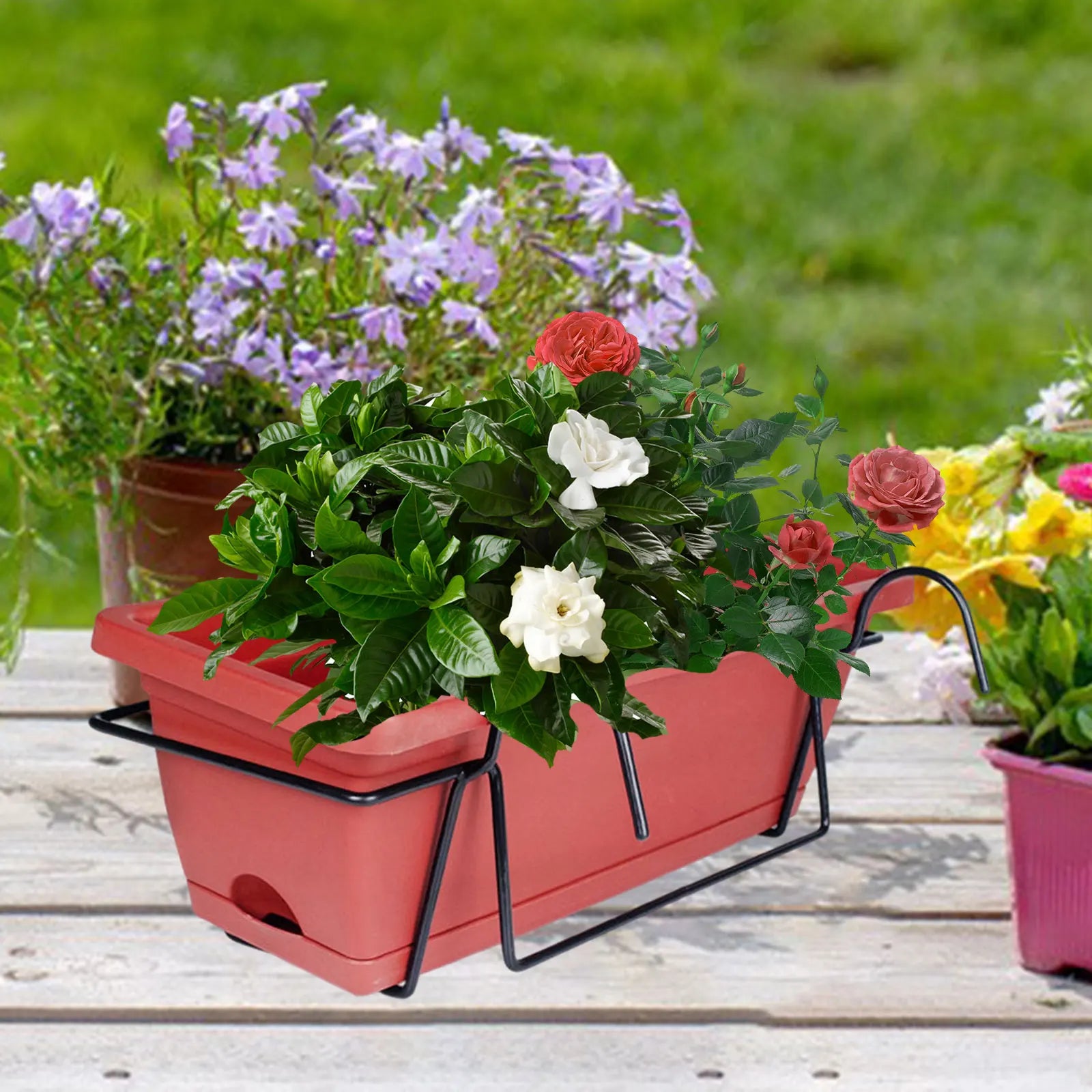 Red rectangular railing planter with greenery and roses on a wooden outdoor surface