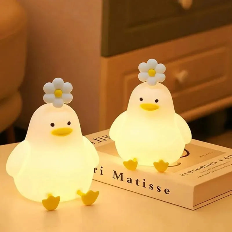 Two silicone duck night lights with daisy accents glowing on a bedside table