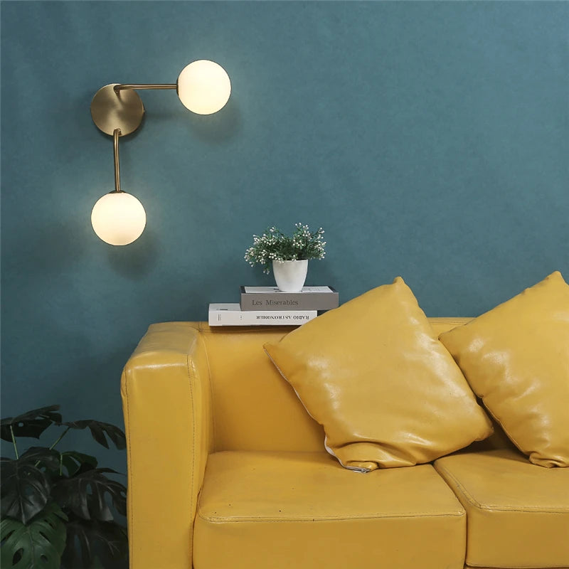 Horizontal double globe wall sconce with brass finish above yellow sofa and books