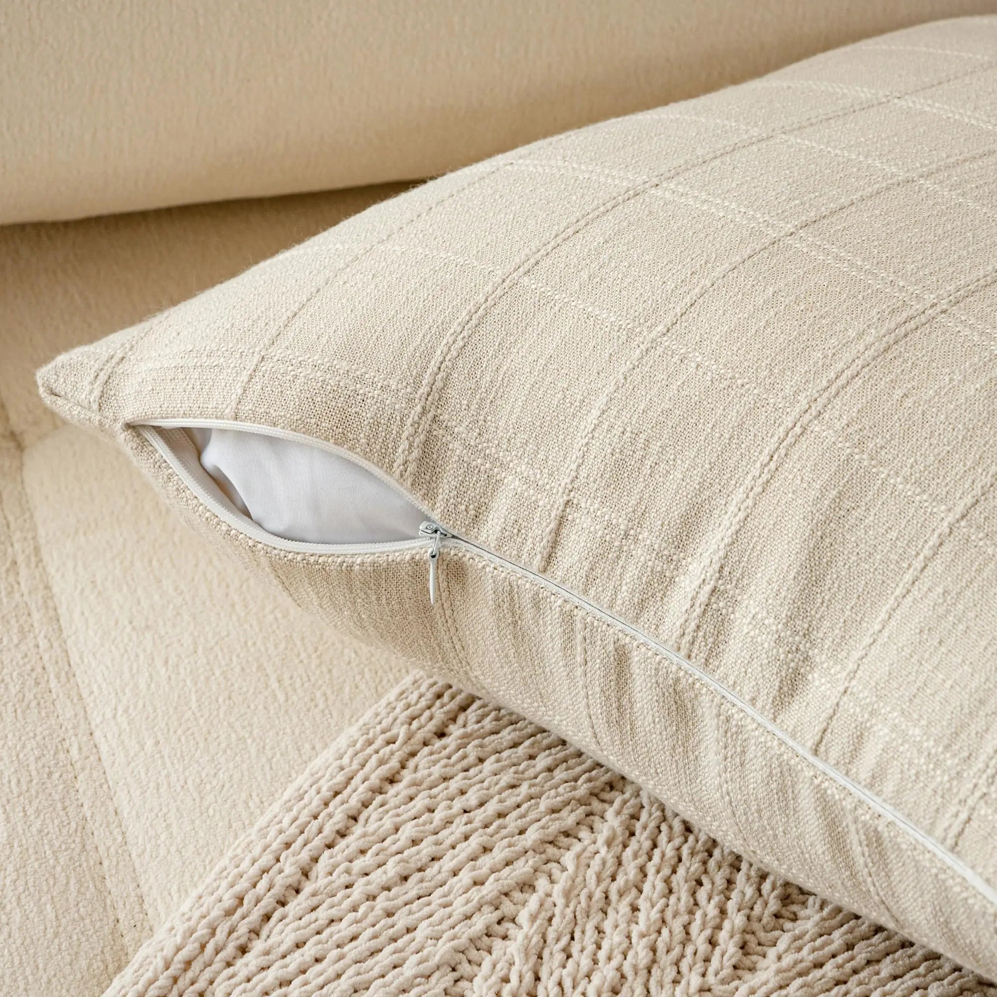 Close-up of beige plaid pillow cover with invisible zipper partially open on a cream couch