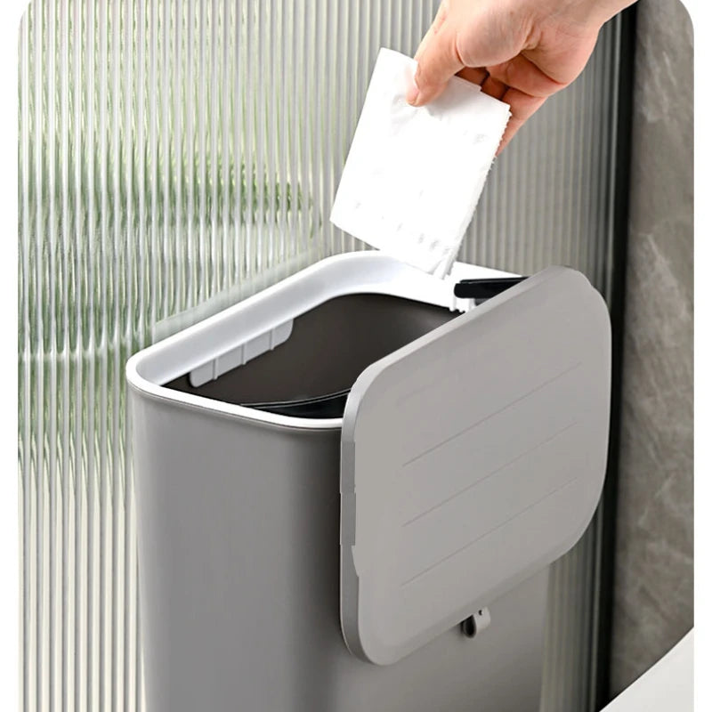 open rectangular trash bin with lid in use, hand throwing away item