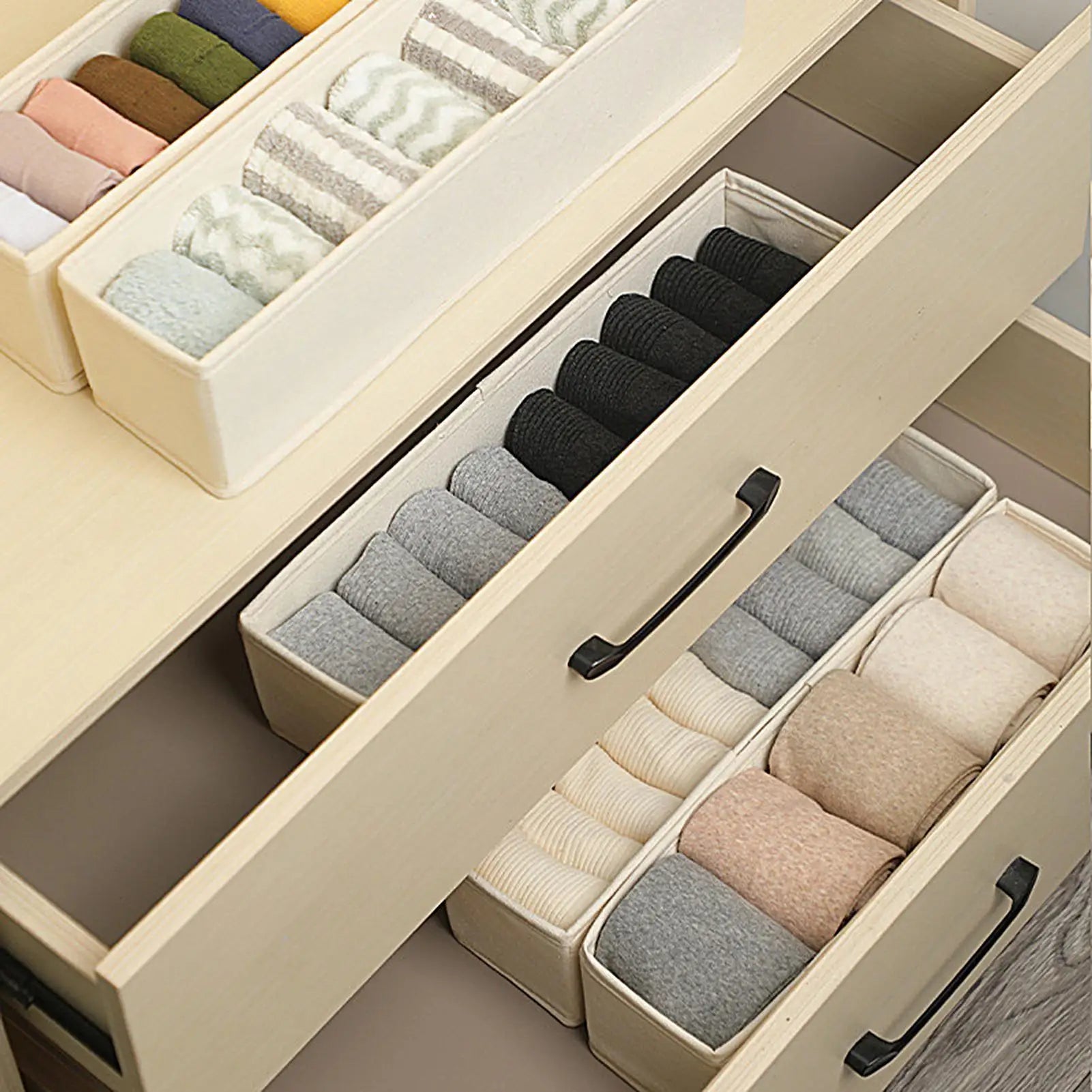 Beige fabric storage bins with socks in a set of open dresser drawers, showing organized compartments