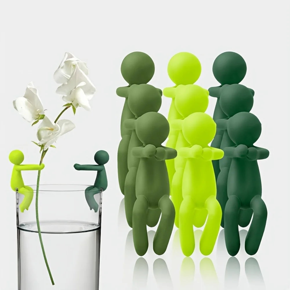 Multiple plant stem holder clips in assorted green tones, two attached to a glass and supporting a flower cutting