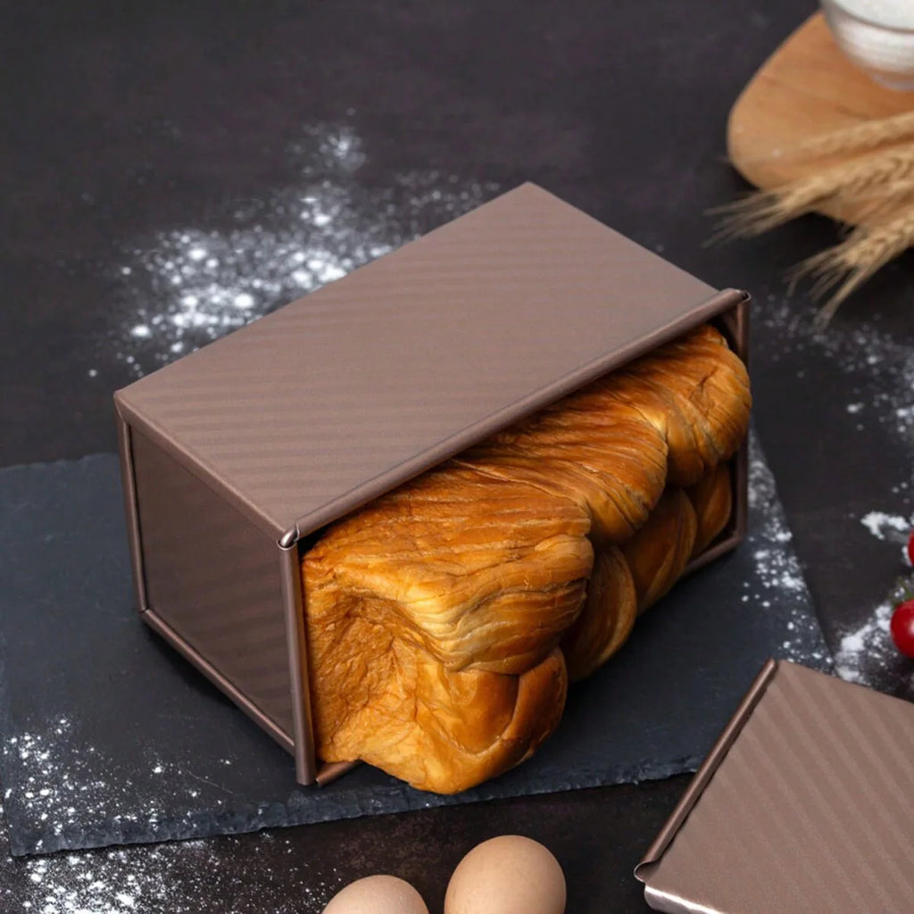 Rectangular carbon steel bread box with golden finish, filled with a baked loaf