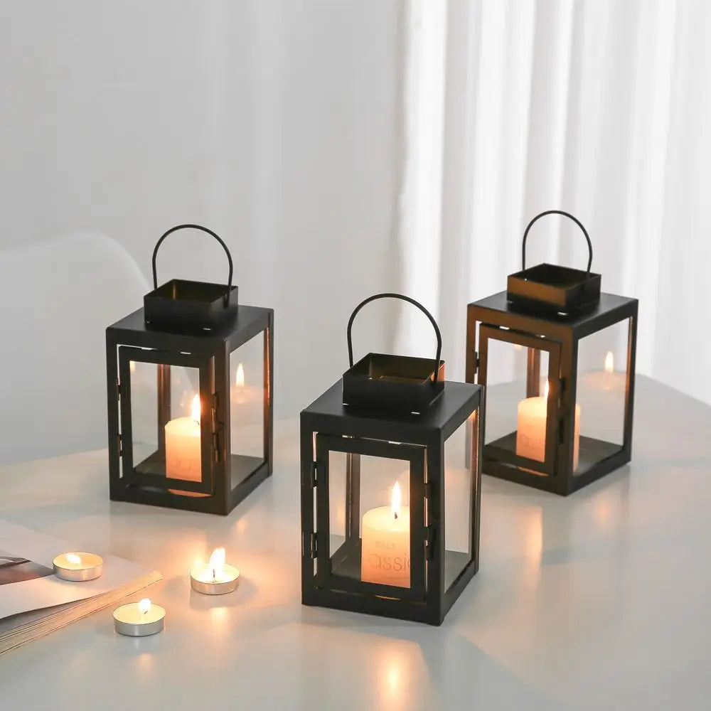 Black iron square candle lanterns with tealight candles glowing on a tabletop