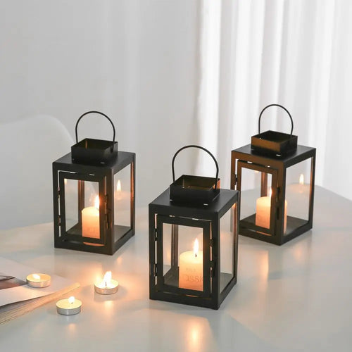 Black iron square candle lanterns with tealight candles glowing on a tabletop