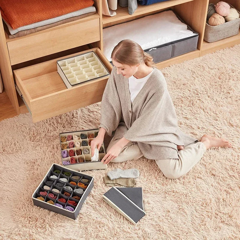 Person sitting on a beige rug sorting socks into gray and beige 24-compartment organizer bins near an open dresser