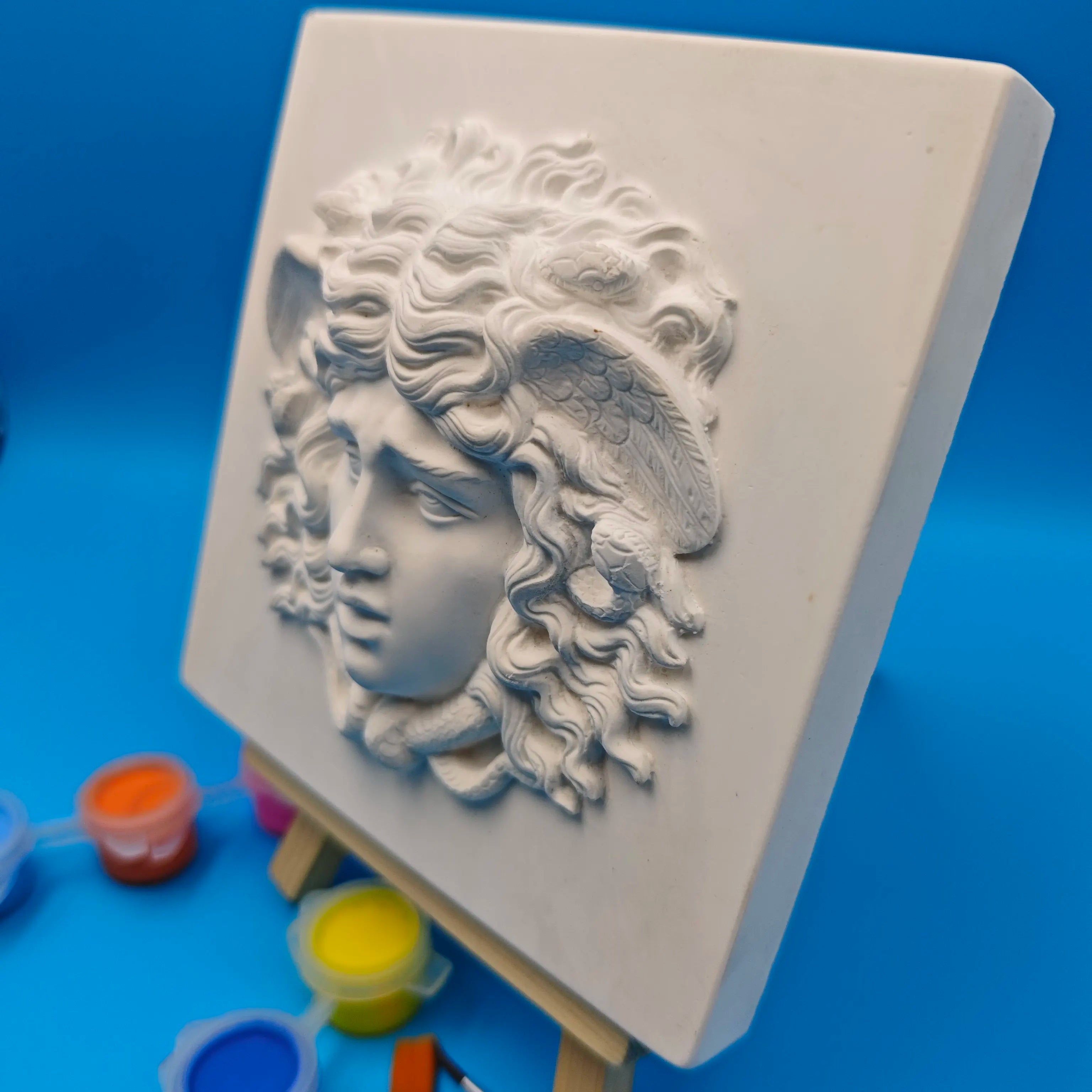 angled side view of Medusa relief sculpture showing raised details and white finish