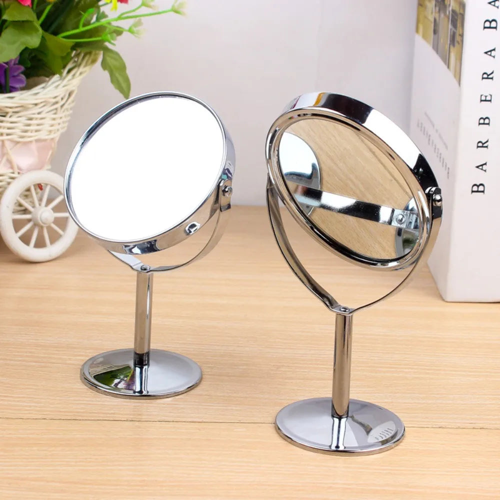 Two double-sided tabletop makeup mirrors with chrome stands shown on a wooden surface