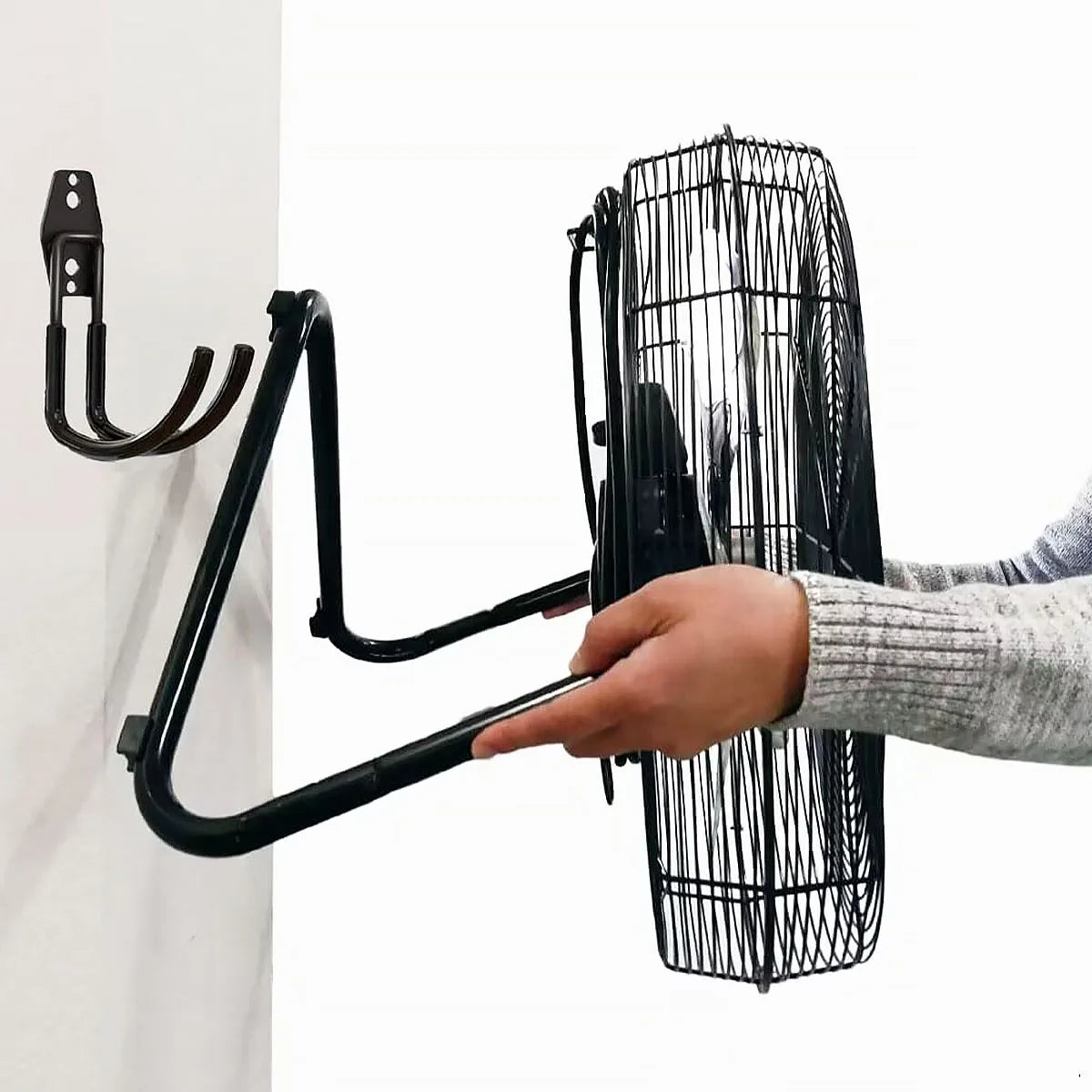 Person placing a large industrial fan onto a black wall-mounted hook installed in a utility room