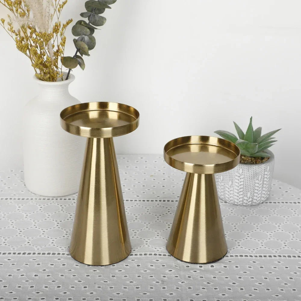 Two gold cone-shaped metal candle holders of different heights side by side, displayed on a table near a vase and succulent.