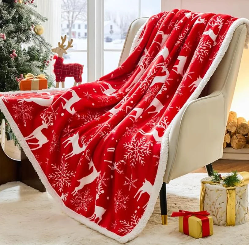 Red sherpa Christmas throw blanket with white reindeer and snowflakes draped over a chair near a holiday tree