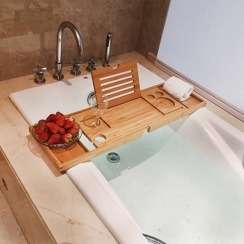 Bamboo bath tray extended across a bathtub holding strawberries, wine glass, towel, and tablet stand.
