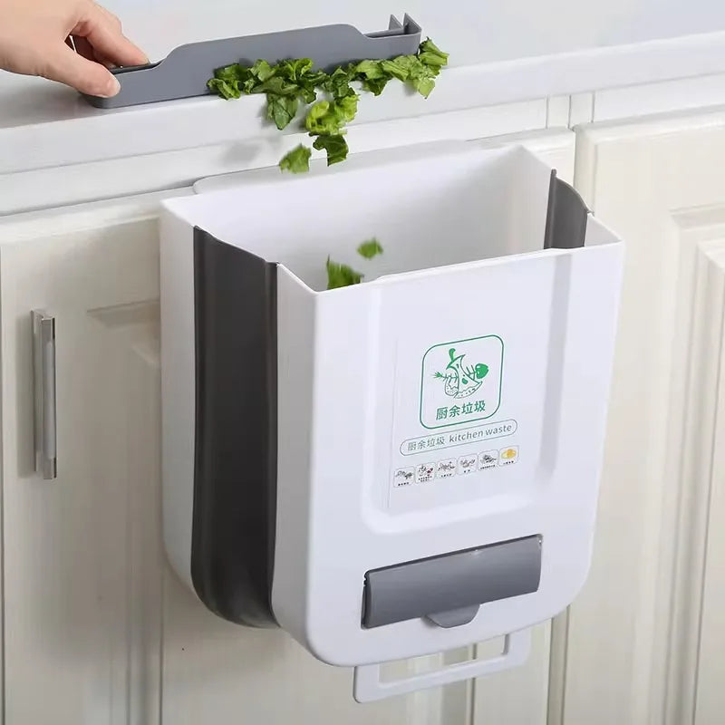 White folding kitchen trash bin mounted to a cabinet door, with chopped lettuce being scraped in