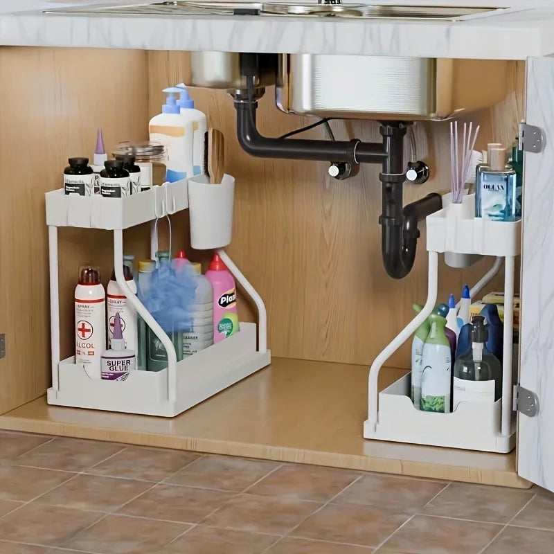 Two white under sink organizers storing bottles and cleaning products under a kitchen sink with visible plumbing