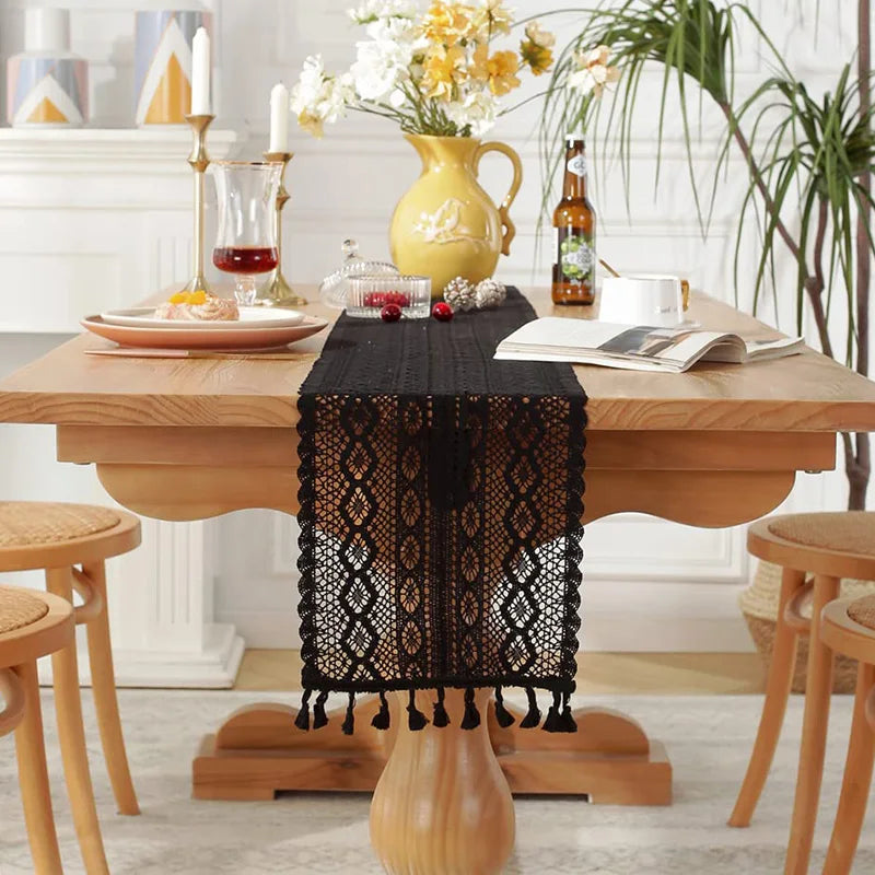 Black crochet lace table runner with tassels styled on a wooden dining table