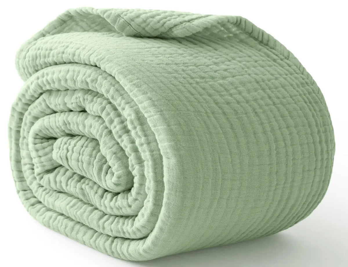 sage green cotton muslin blanket rolled up on a white surface