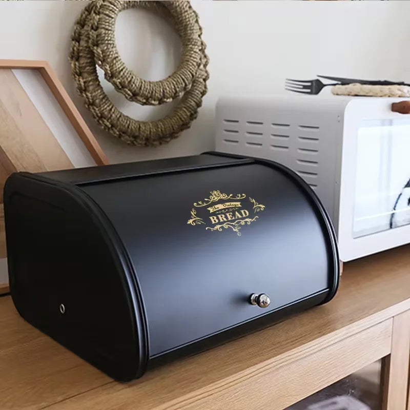 Black metal bread box with gold decorative print on a kitchen counter