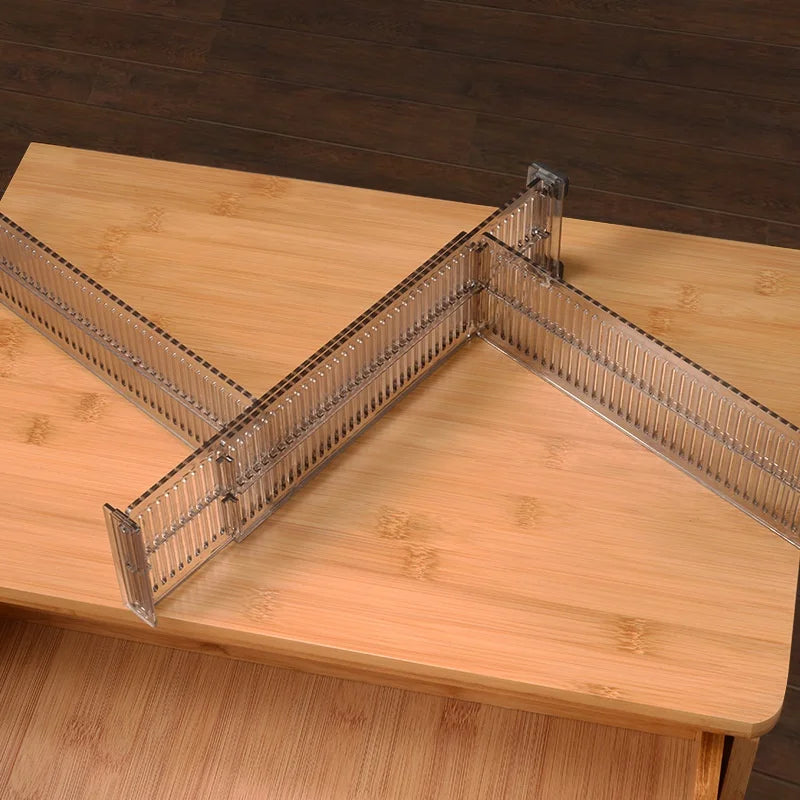 Two adjustable clear drawer dividers arranged in an L-shape on a wooden surface