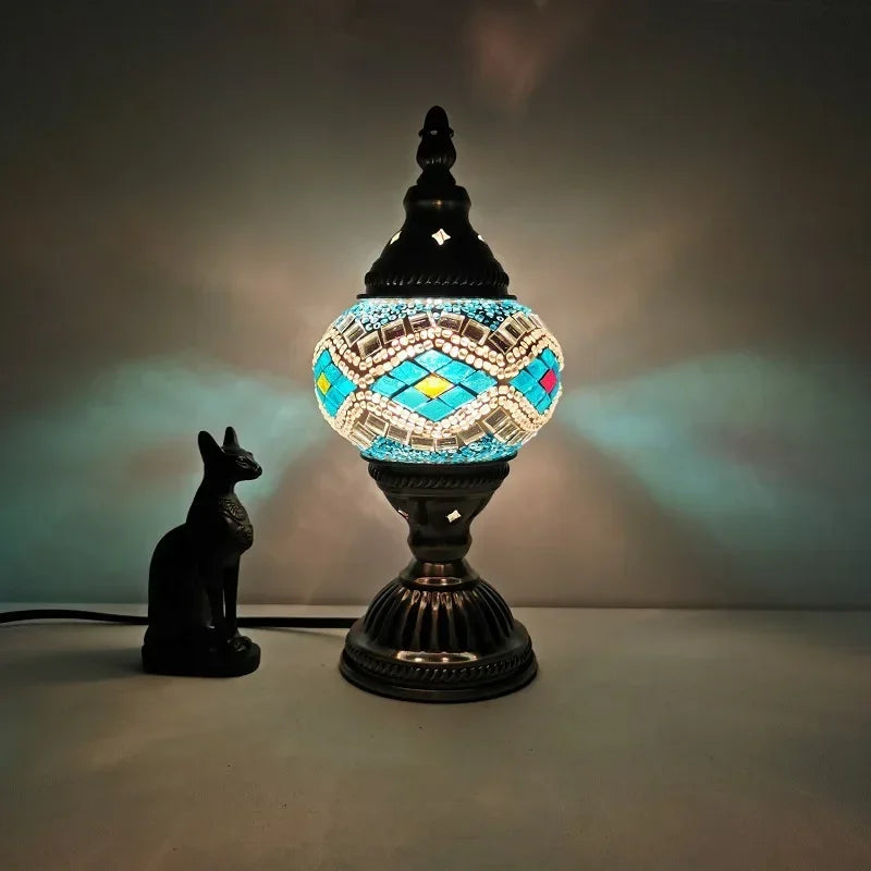 Stained glass mosaic table lamp with geometric blue and white design lit up on a desk
