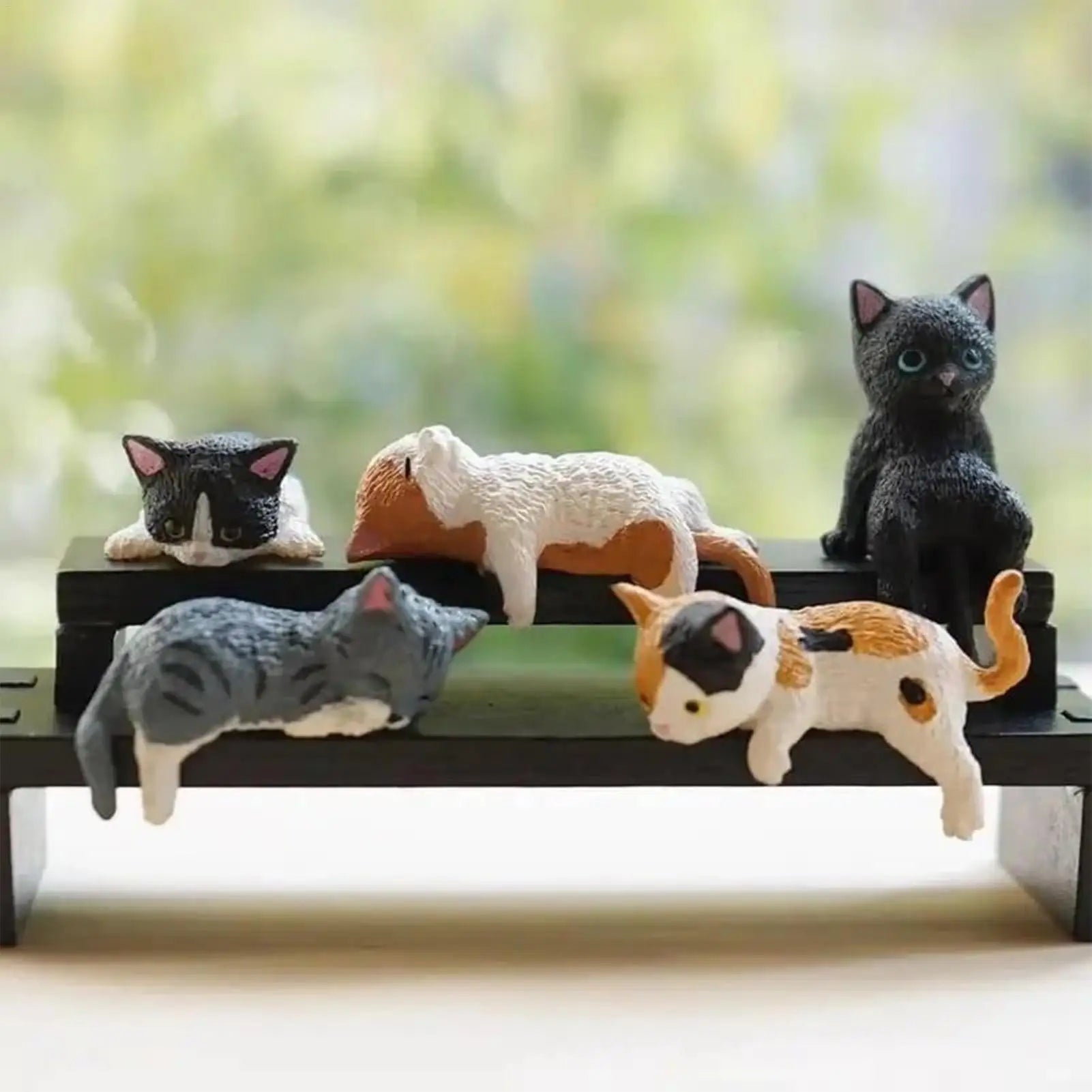 Five small cat figurines arranged on a shelf or tabletop, creating a playful vignette