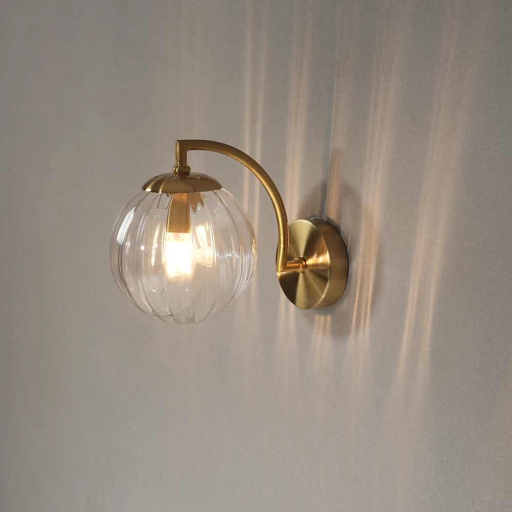Ribbed glass wall sconce with brass arm and clear glass globe shade illuminated against a neutral wall