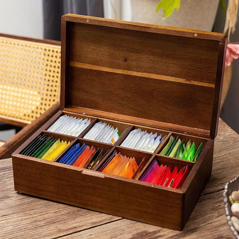 Acacia wood tea bag organizer with 8 compartments filled with assorted tea packets on a kitchen table
