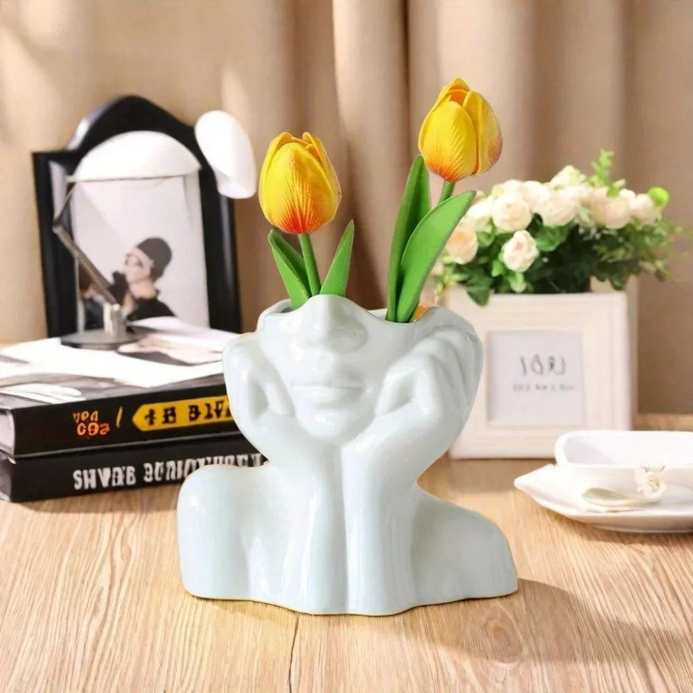 Face sculpture holder with yellow tulips, placed on a desk with books and decor