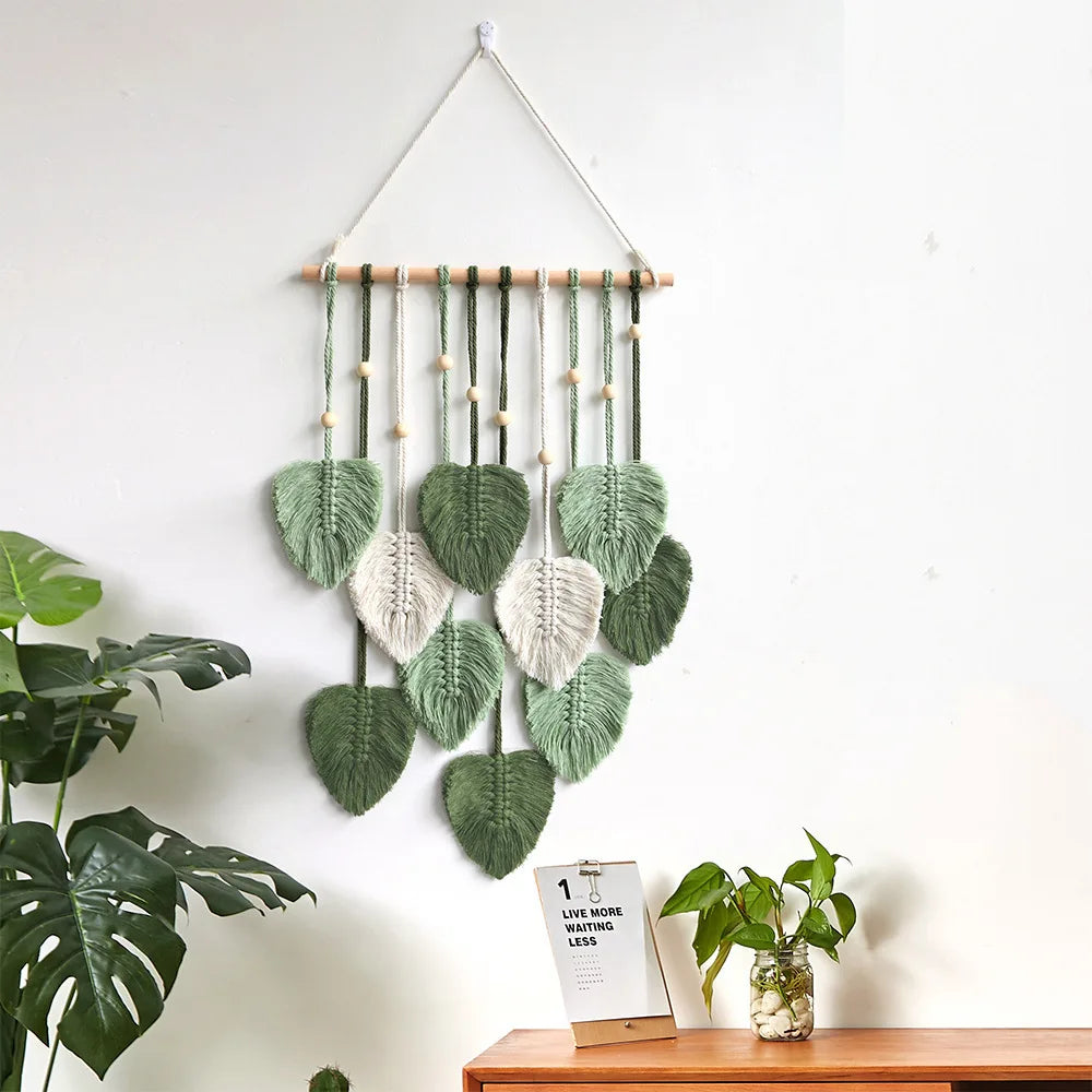 Green leaf woven tapestry wall hanging displayed above a plant and wooden cabinet