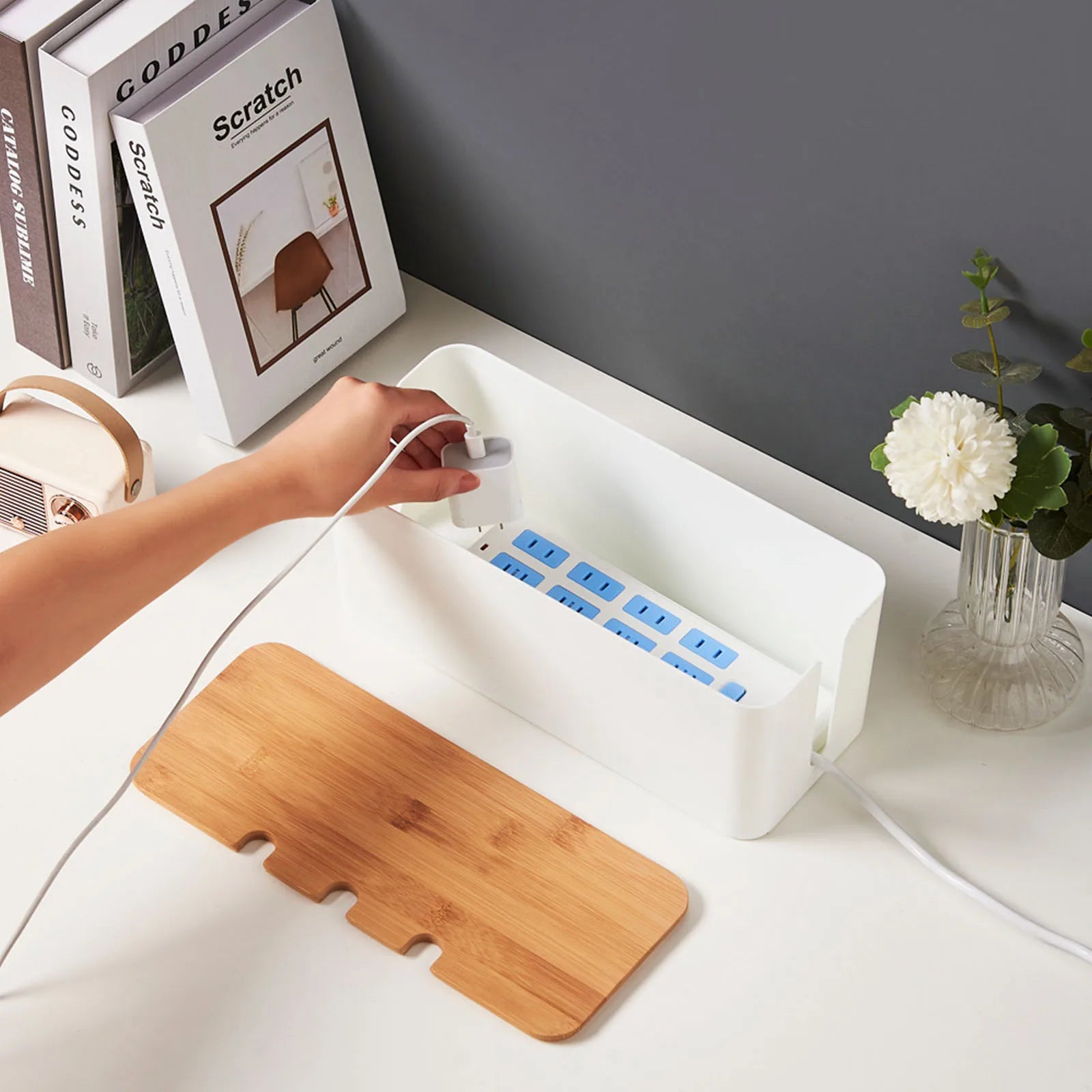 Hand placing plug inside white cable management box with removable wood-style lid